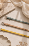 Three leather belts in green, brown, and yellow on a textured surface.