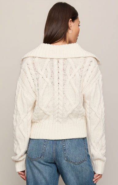 Person wearing a cream knitted cardigan and blue jeans on a plain background