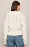 Person wearing a cream knitted cardigan and blue jeans on a plain background