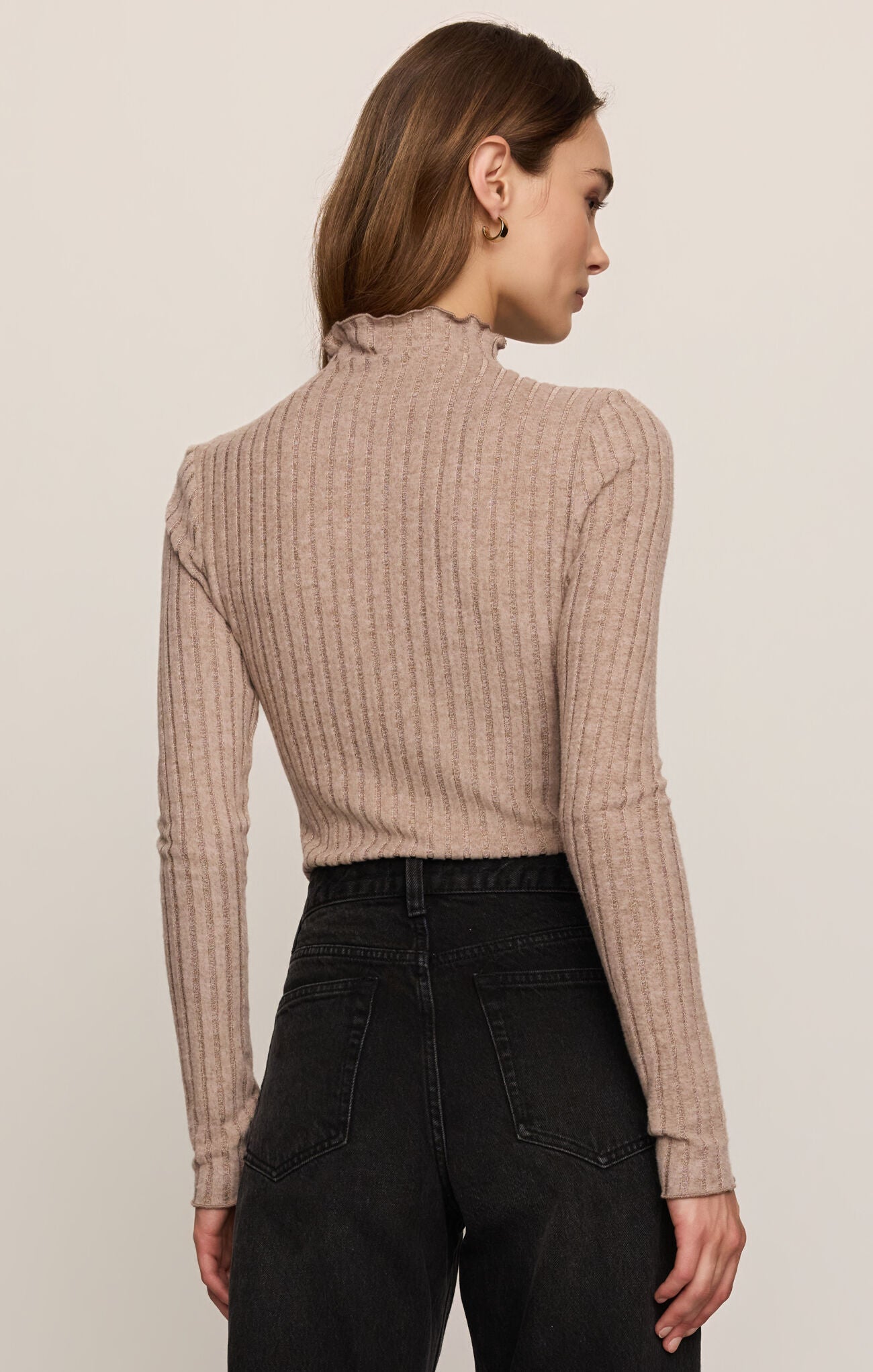 Woman wearing a beige ribbed sweater and black pants against a plain background