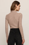Woman wearing a beige ribbed sweater and black pants against a plain background