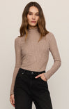 Woman wearing a brown ribbed turtleneck sweater and black pants against a beige background