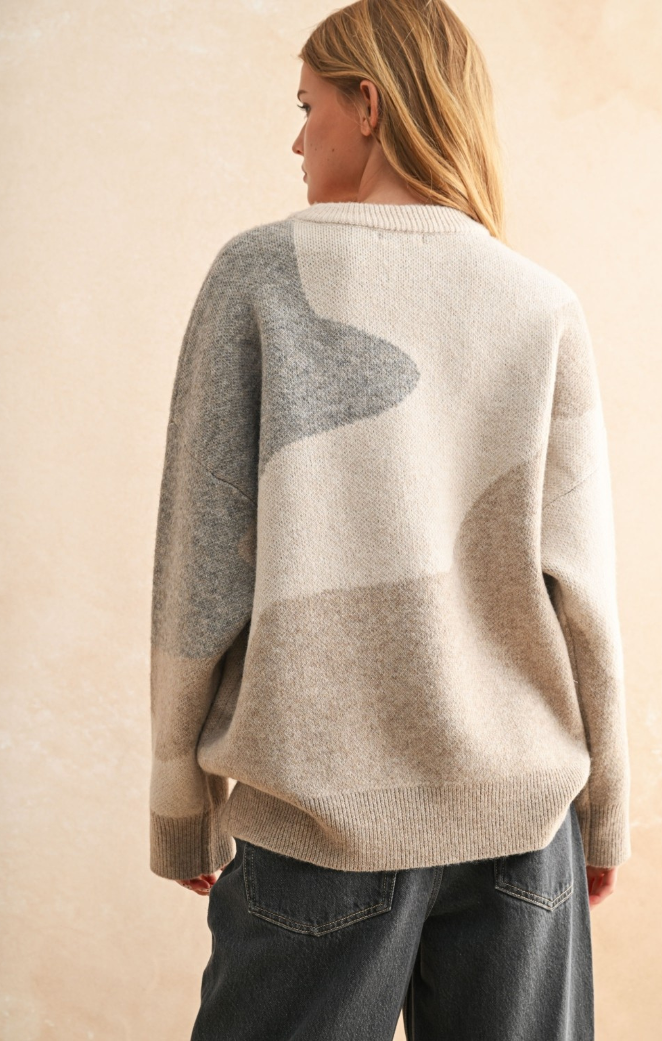 Person wearing a beige and gray patterned sweater against a beige background