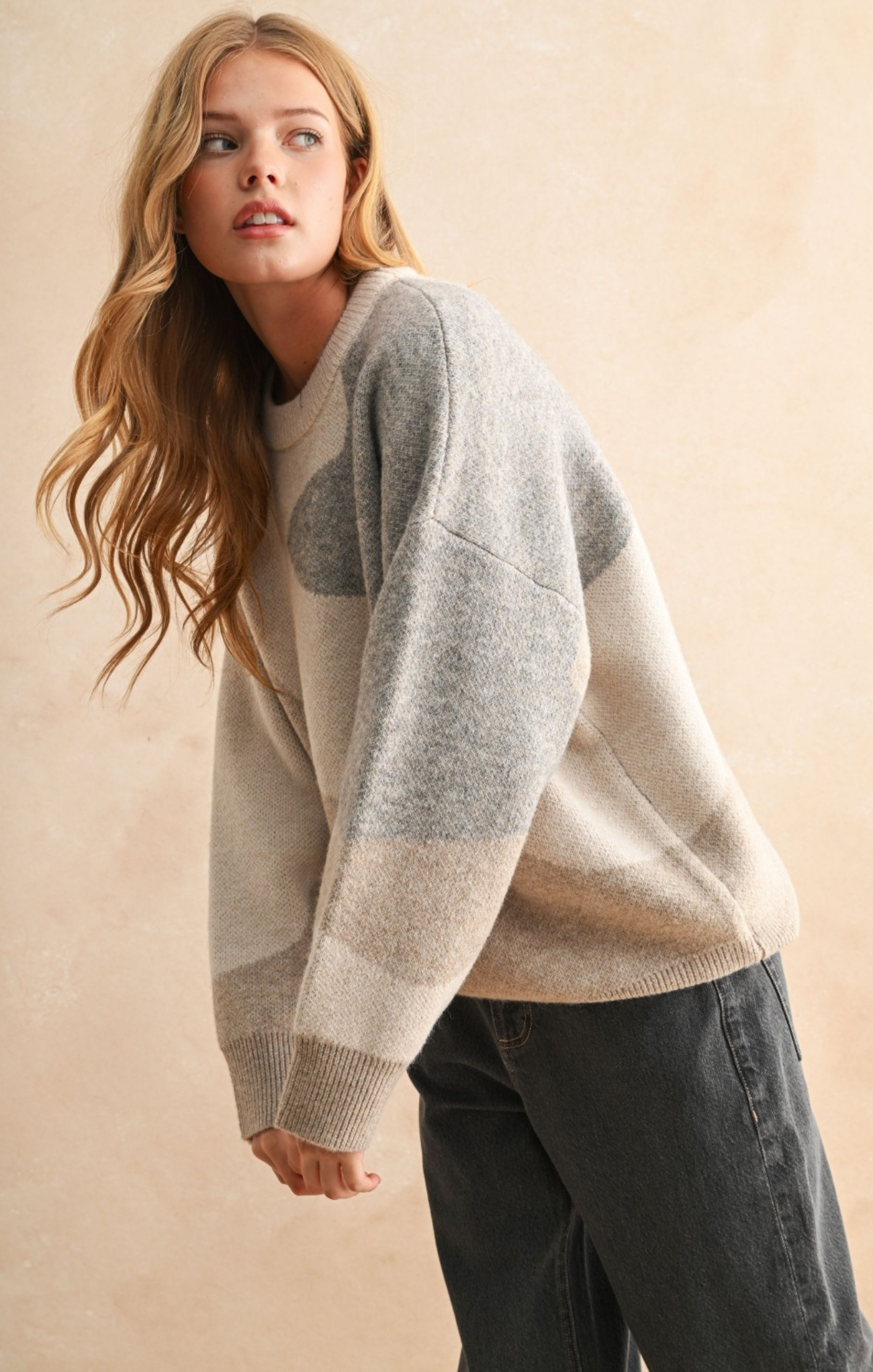 Woman wearing a gray and beige sweater against a beige background