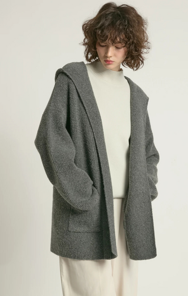 Person wearing a gray hooded cardigan over a white top on a plain background