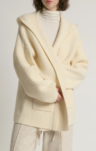 Person wearing a light yellow cardigan over a white turtleneck on a plain background