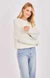 Woman wearing a cream chunky knit sweater and light blue jeans on a white background