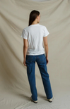 A model shown from the back wearing a white short-sleeve t-shirt and blue jeans, standing against a draped beige fabric backdrop.