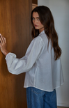 Woman wearing a light blue shirt and blue jeans standing against a wooden door.