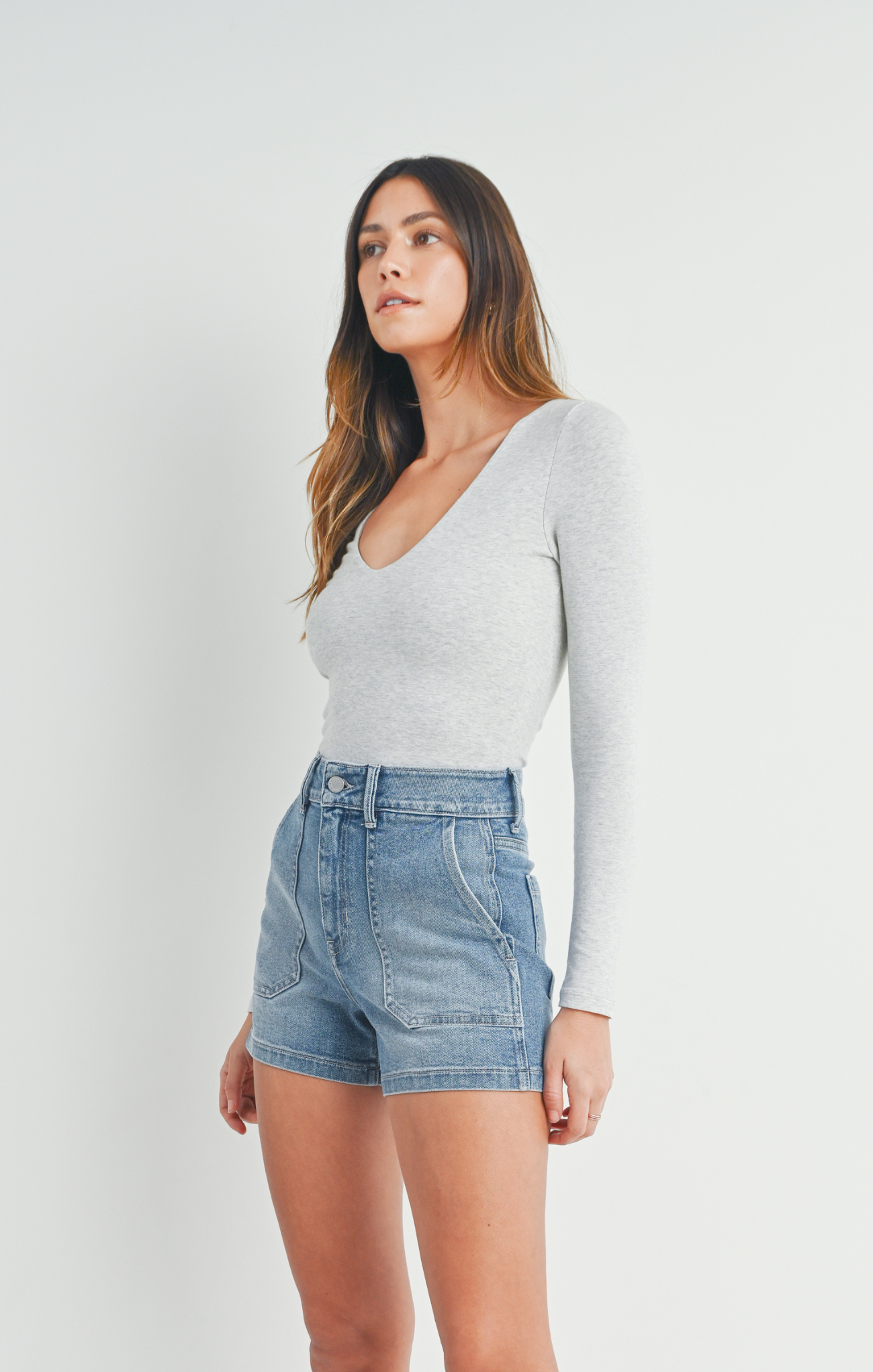Woman wearing a light gray long-sleeve top and denim shorts on a white background