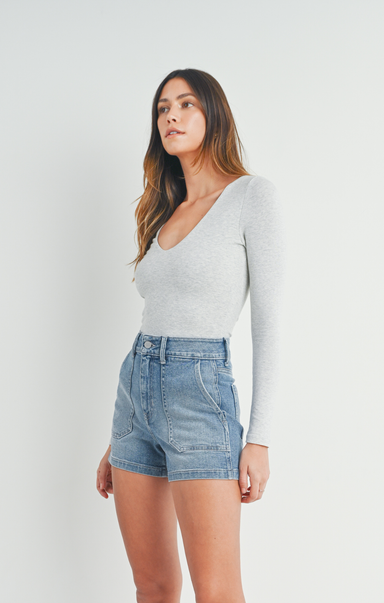 Woman wearing a light gray long-sleeve top and denim shorts on a white background
