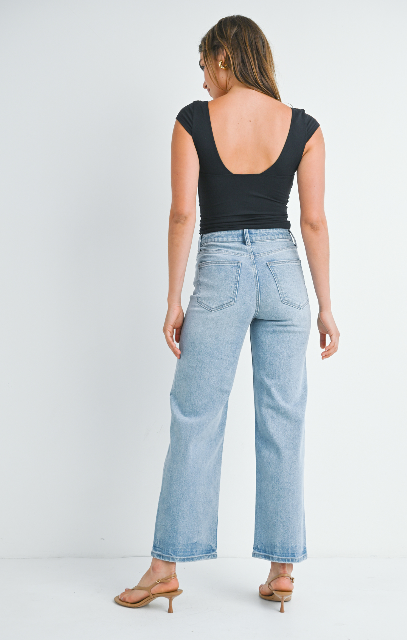 Woman wearing light blue jeans and a black top on a white background