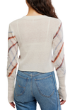A woman shown from the back wearing a cream-colored knit sweater with patterned sleeves in orange, blue, and white, paired with blue jeans against a white background.