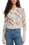 A woman wearing a cream-colored knit cardigan with a rust-orange and light blue plaid pattern, paired with blue jeans, shown against a plain white background.