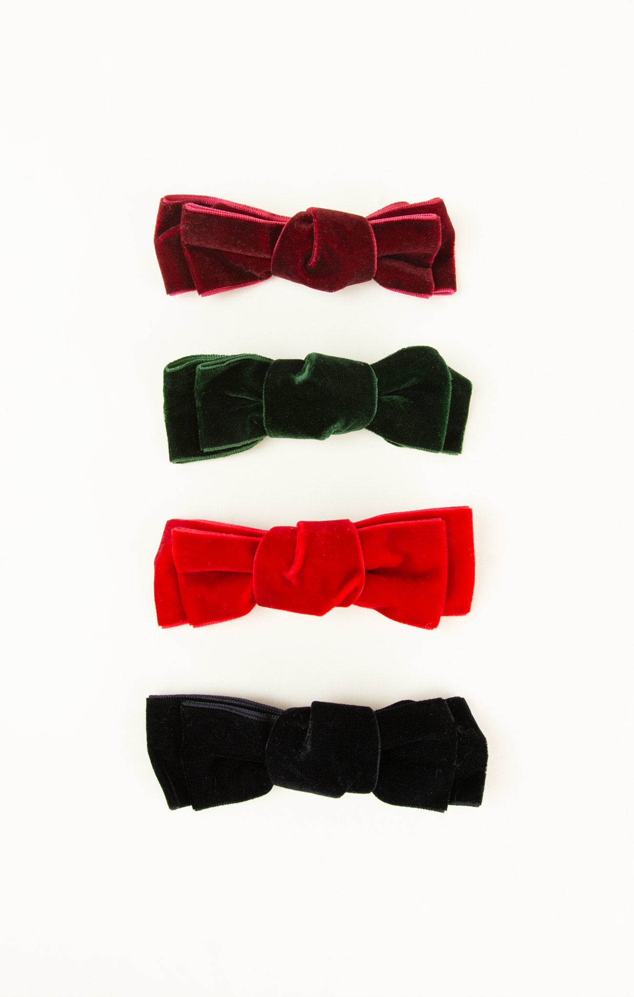 Four velvet hair bows in red, green, black, and red on a white background