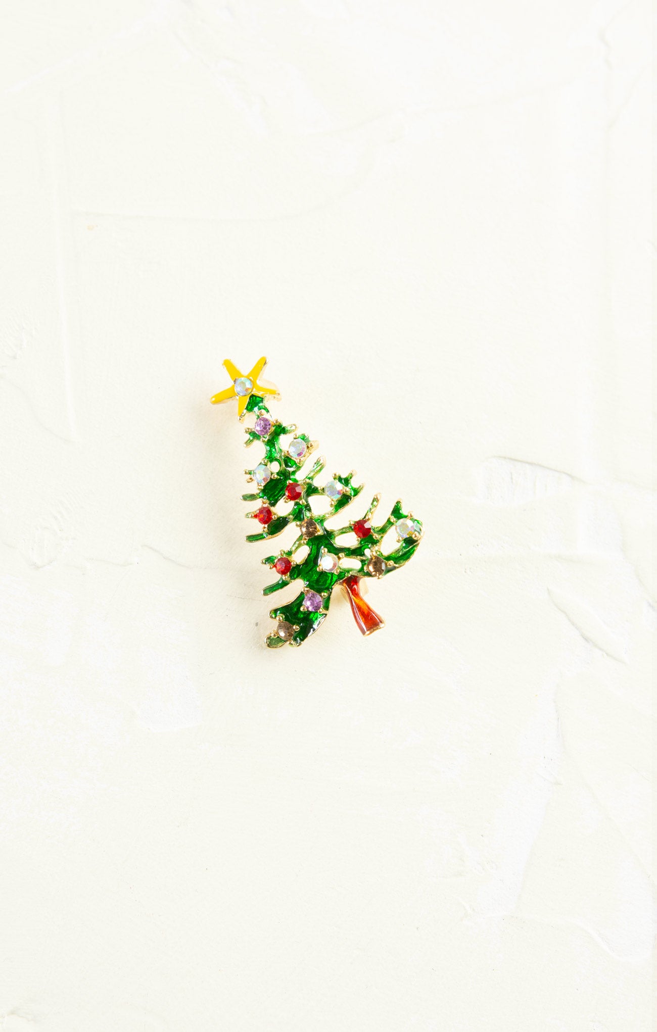 Christmas tree-shaped brooch with green leaves, red berries, and gold stars on a white background