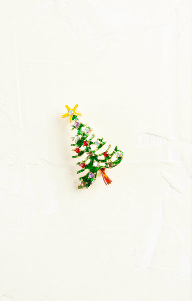 Christmas tree-shaped brooch with green leaves, red berries, and gold stars on a white background