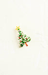 Christmas tree-shaped brooch with green leaves, red berries, and gold stars on a white background