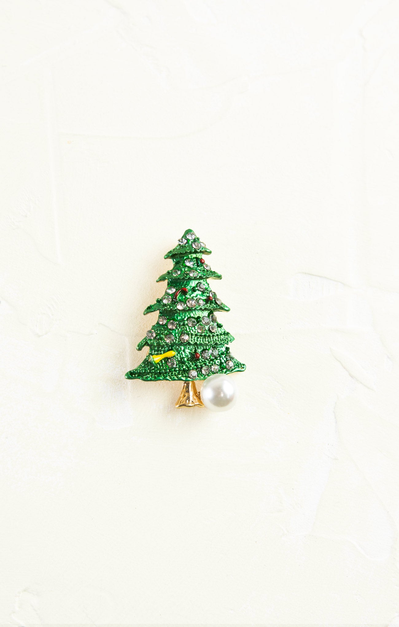 Green Christmas tree-shaped brooch with a pearl on a white background
