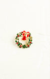 Christmas-themed brooch with a wreath and Santa Claus figure on a white background