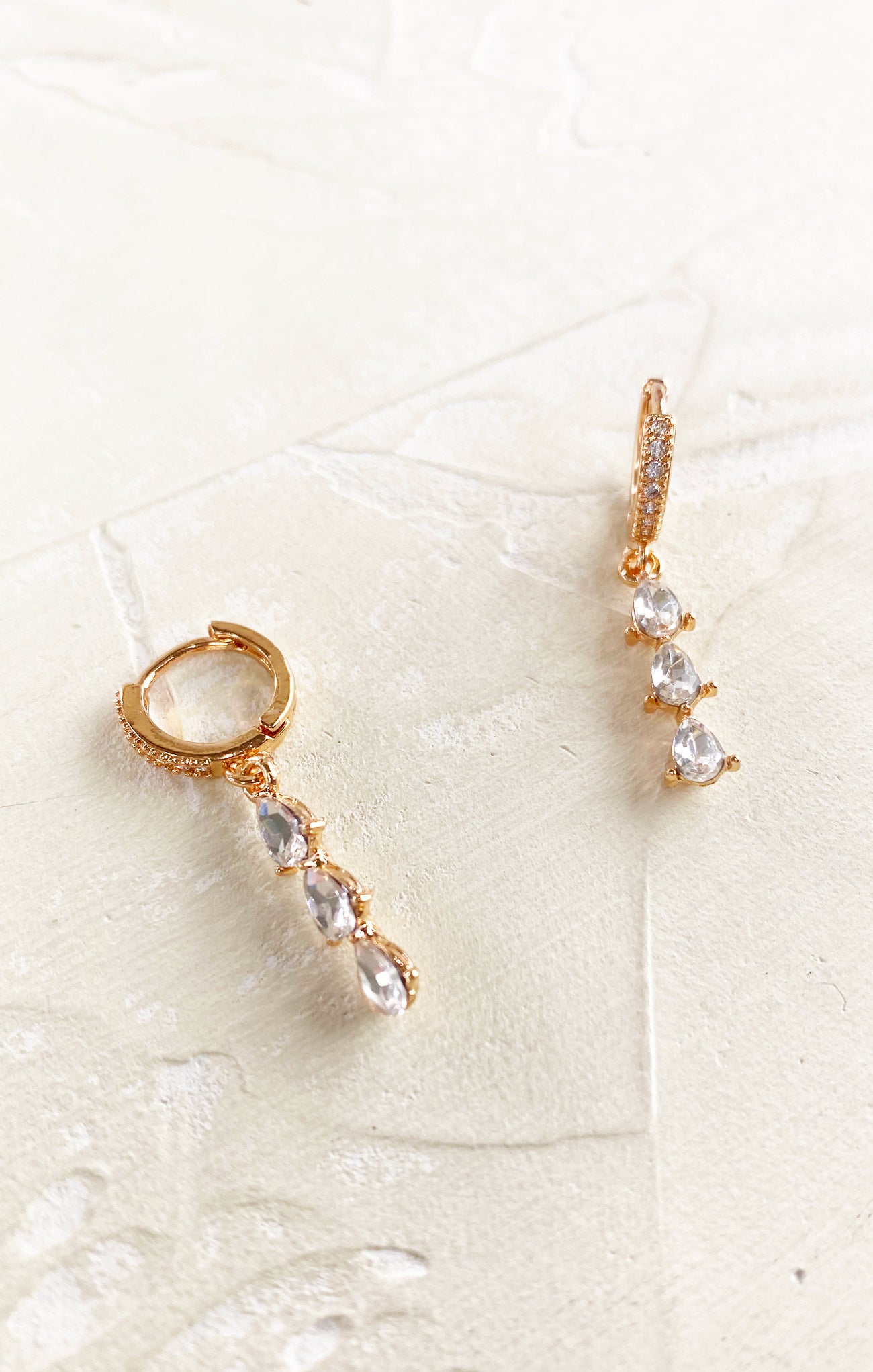 Gold earrings with pearl-like stones on a textured white surface