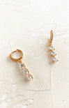 Gold earrings with pearl-like stones on a textured white surface