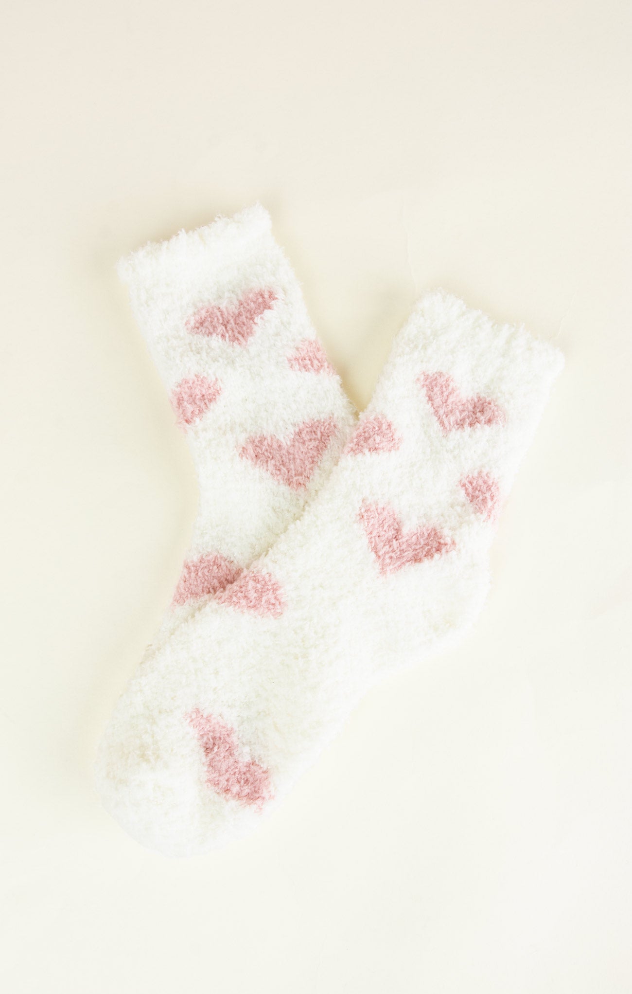 Pair of white socks with pink heart patterns on a light beige background