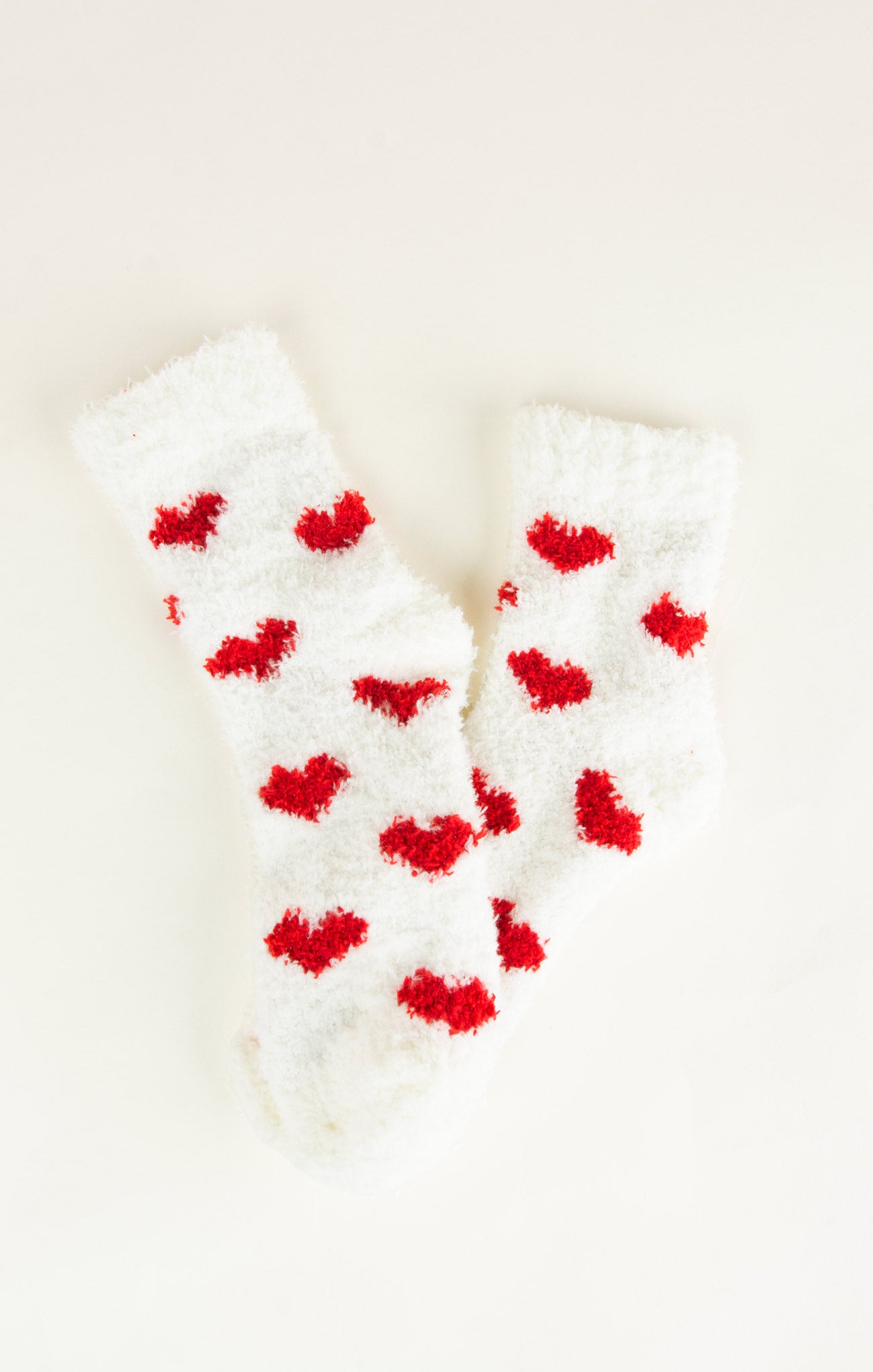 White fuzzy socks with red heart patterns on a light beige background