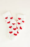 White fuzzy socks with red heart patterns on a light beige background