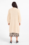 Woman wearing a long beige cardigan over a floral dress on a white background