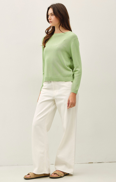 Woman wearing a light green sweater and white pants on a plain background
