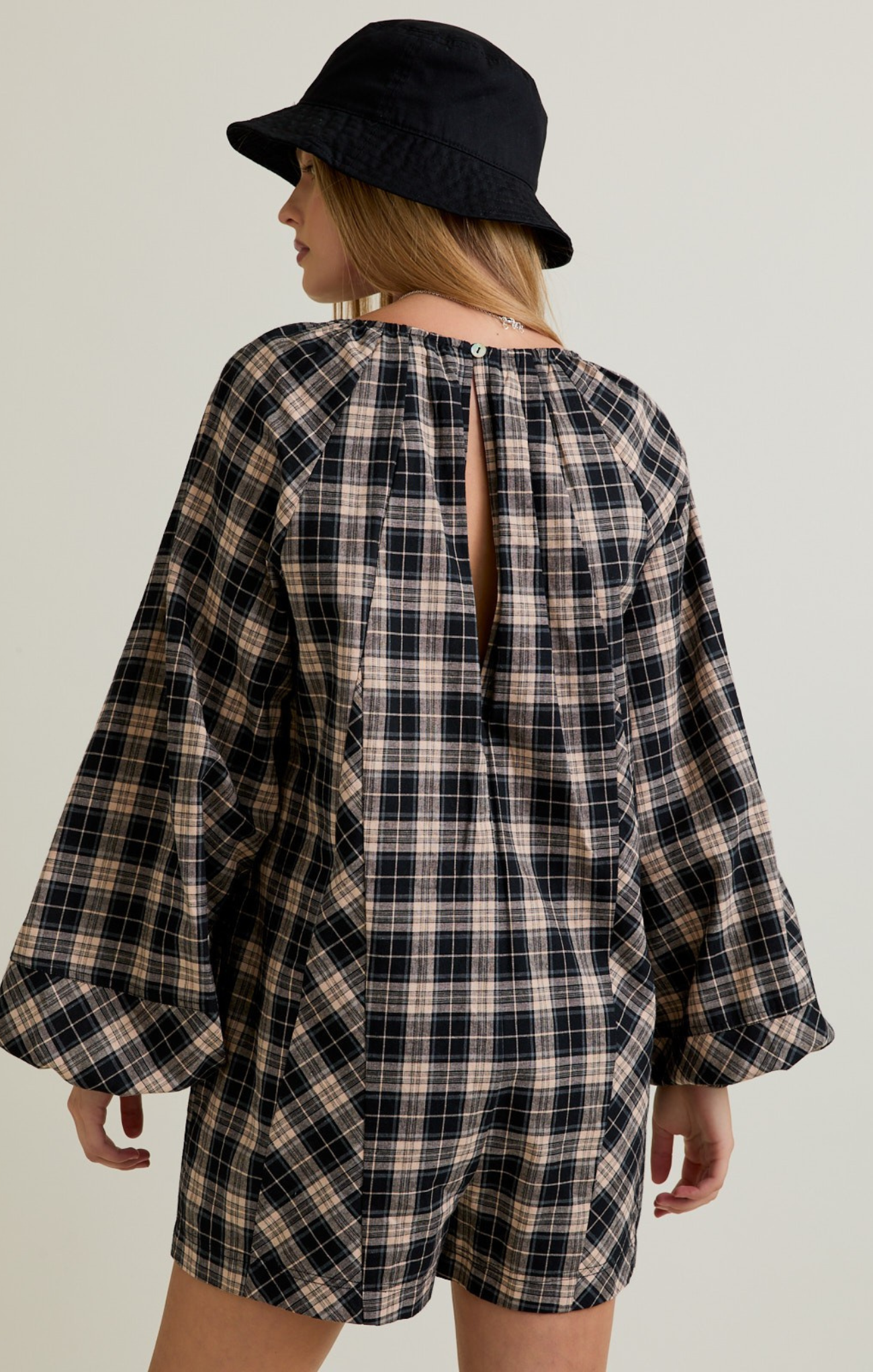 Person wearing a plaid dress with a black hat on a plain background