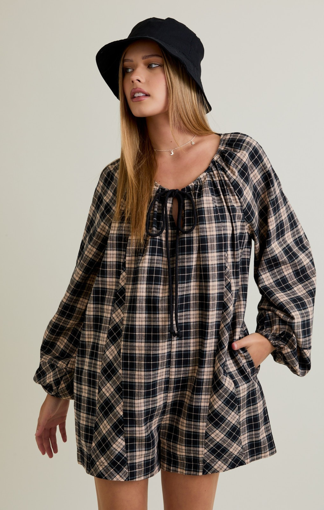 Woman wearing a plaid dress and black hat against a plain background