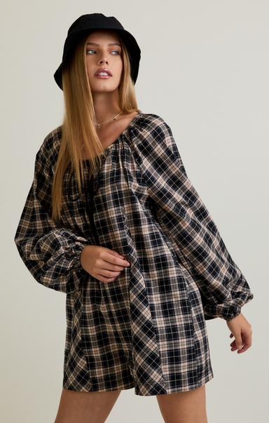Woman wearing a plaid dress and black hat against a plain background