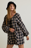 Woman wearing a plaid dress and black hat against a plain background