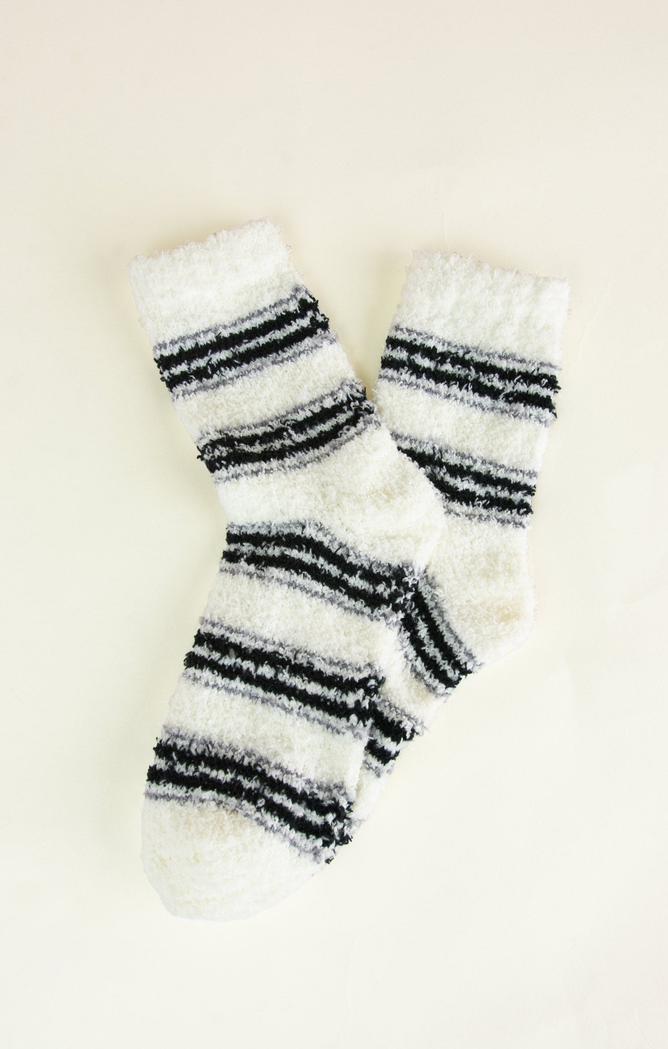 Pair of white fuzzy socks with black stripes on a light beige background