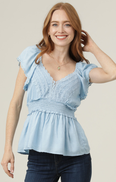 Woman wearing a light blue top with ruffled sleeves against a beige background