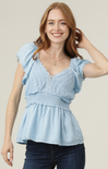 Woman wearing a light blue top with ruffled sleeves against a beige background