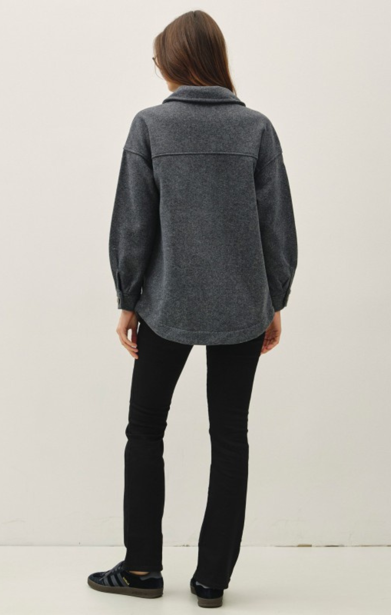 Person wearing a gray jacket and black pants on a white background