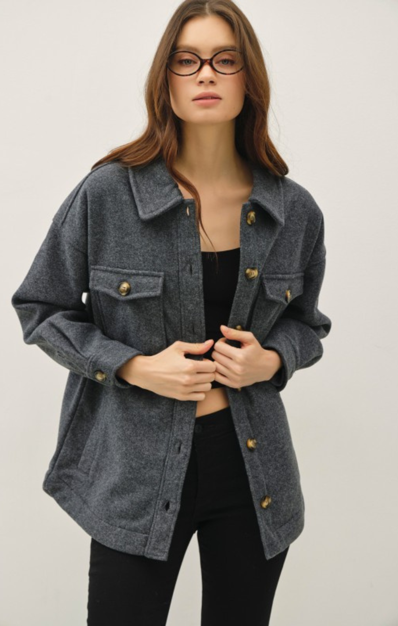 Woman wearing a gray denim jacket with gold buttons on a plain background