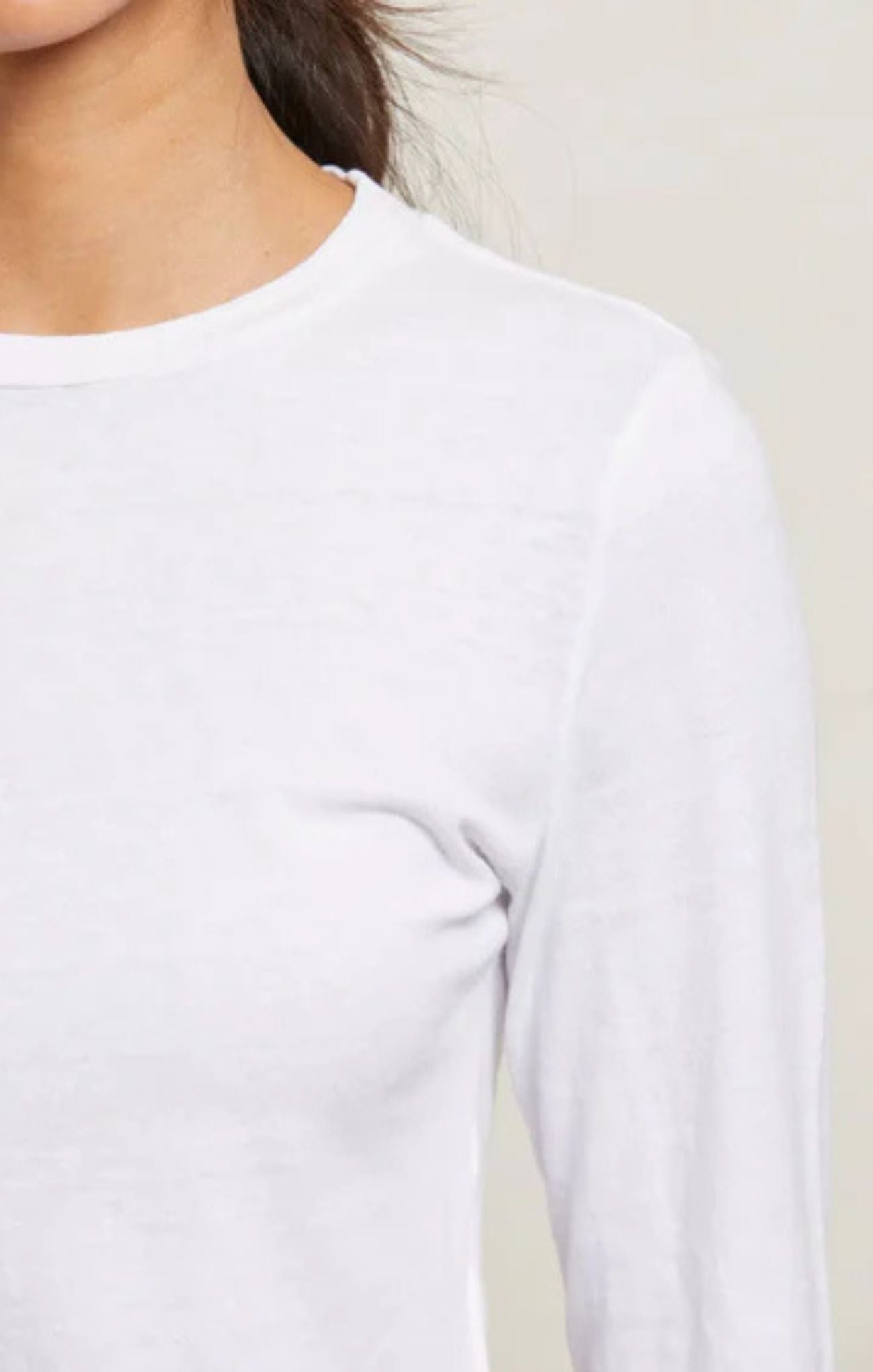 Close-up of a person wearing a plain white long-sleeve crew-neck top against a light neutral background.