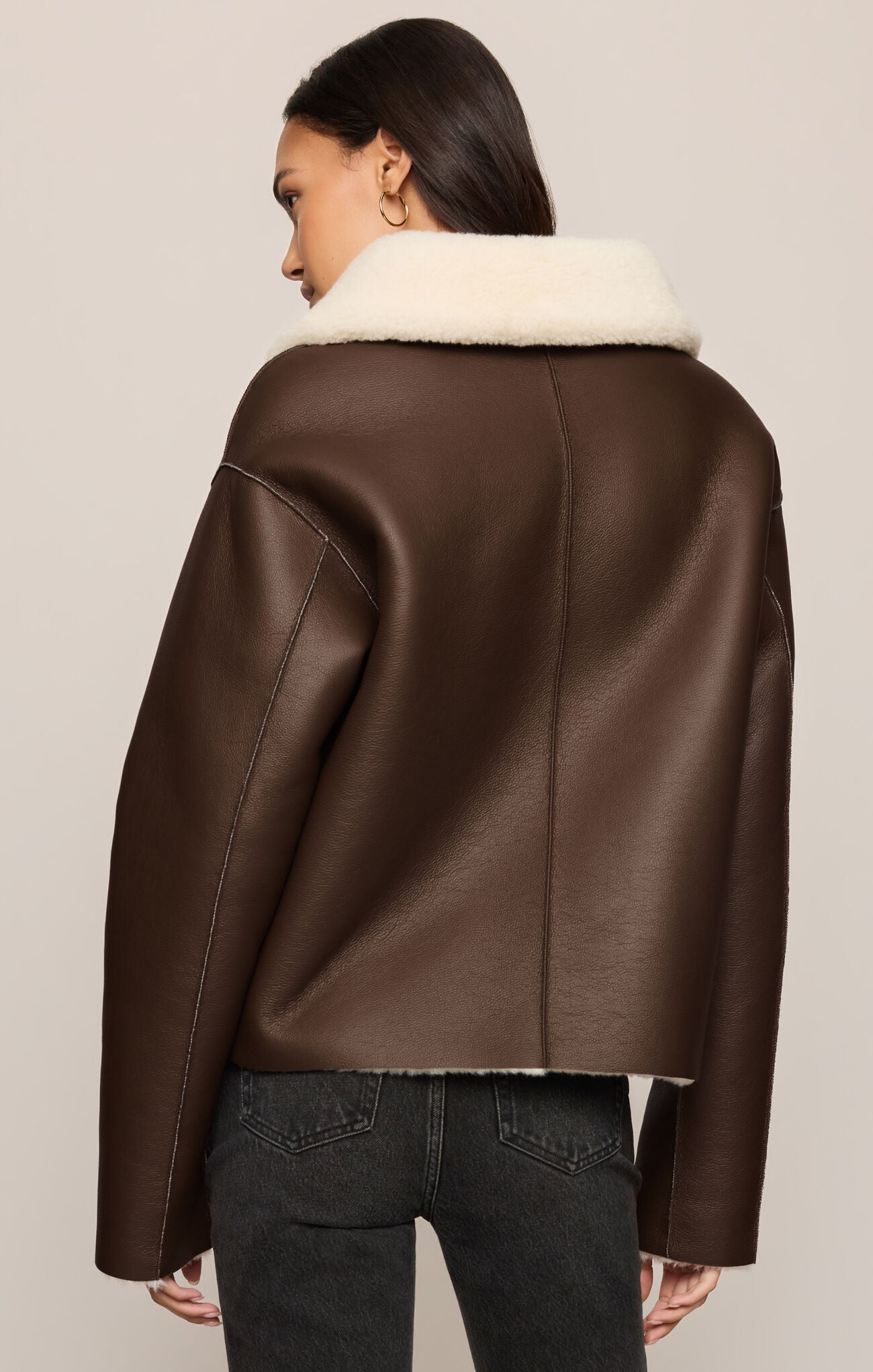 Brown leather jacket with white fur lining worn by a person on a beige background