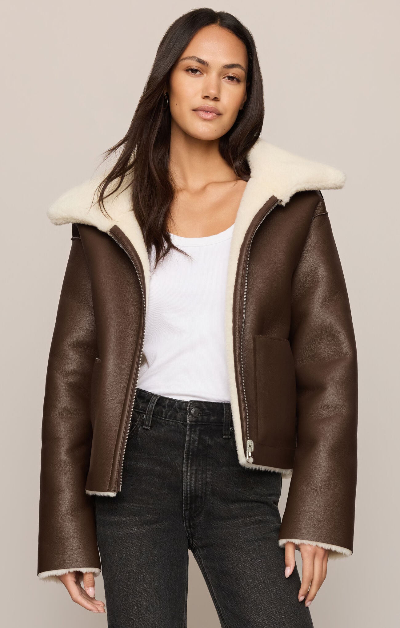 Woman wearing a brown leather jacket with white fur lining on a plain background