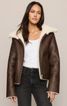 Woman wearing a brown leather jacket with white fur lining on a plain background
