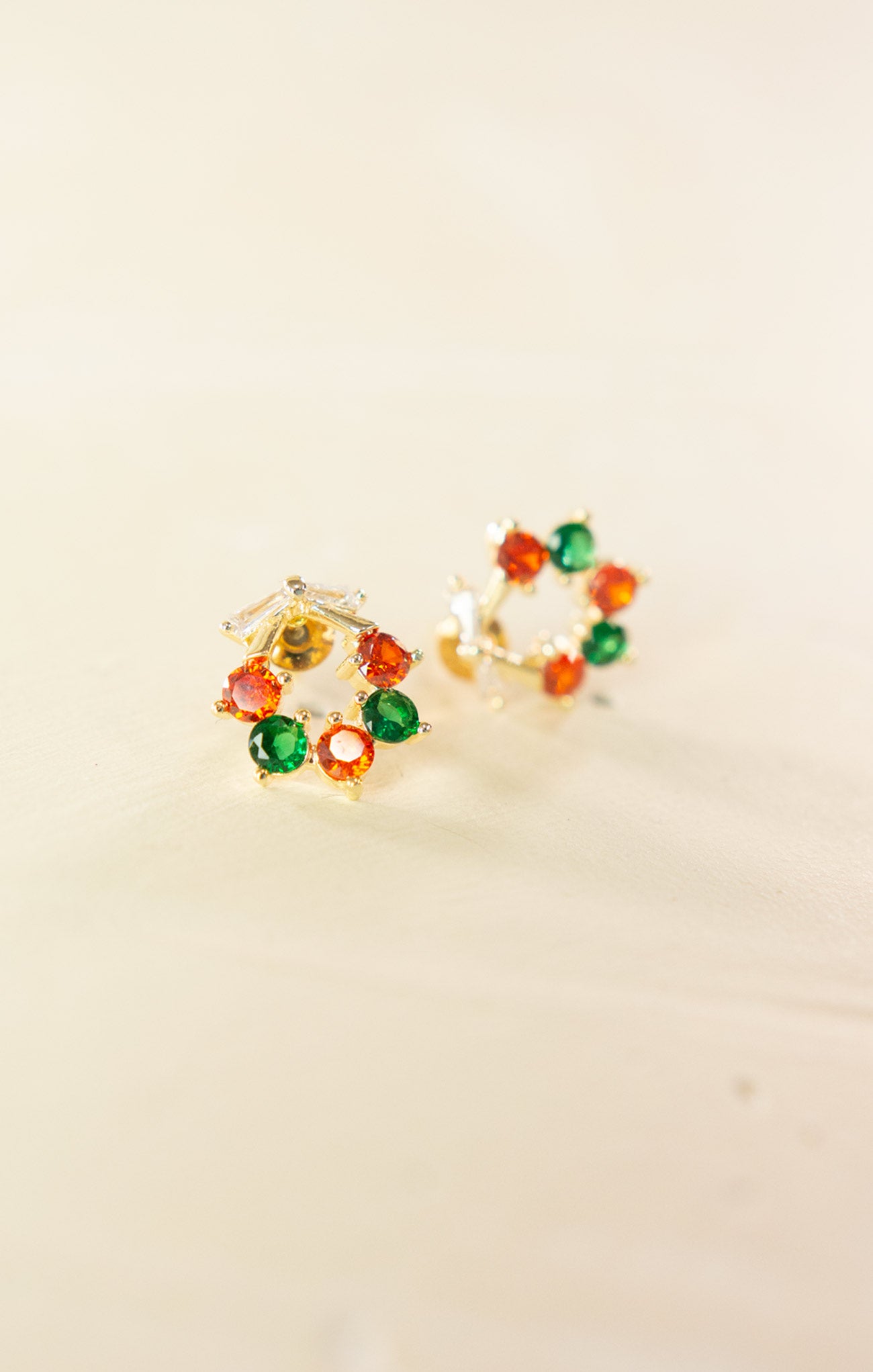 Pair of earrings with colorful gemstones on a beige background
