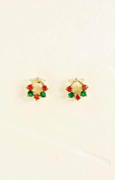 Gold hoop earrings with red and green gemstones on a beige background