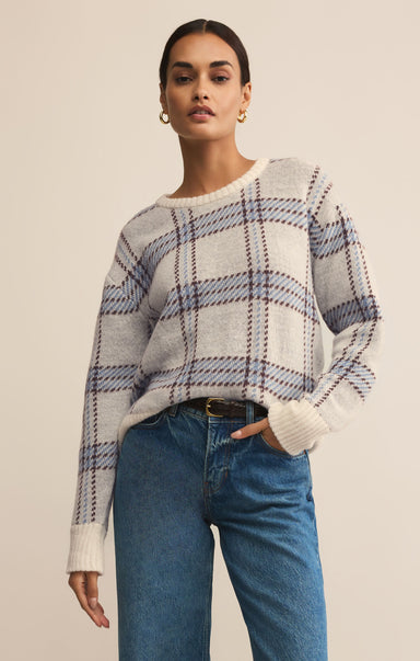 Woman wearing a plaid sweater and blue jeans against a beige background