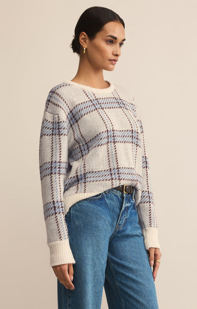 Woman wearing a plaid sweater and blue jeans against a beige background