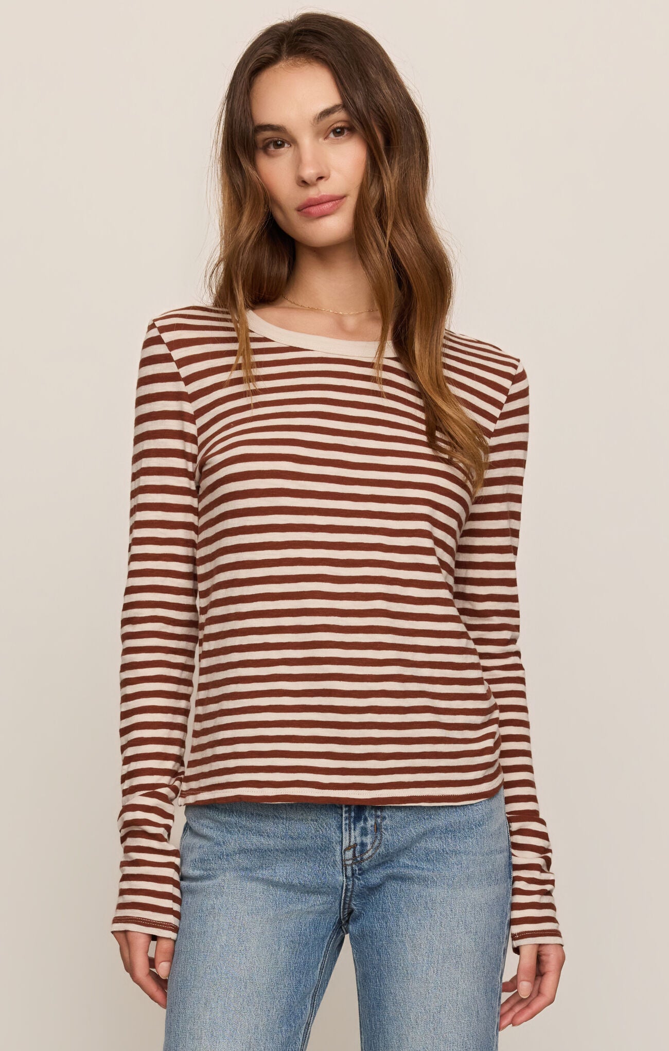 Woman wearing a striped long-sleeve top and jeans against a plain background