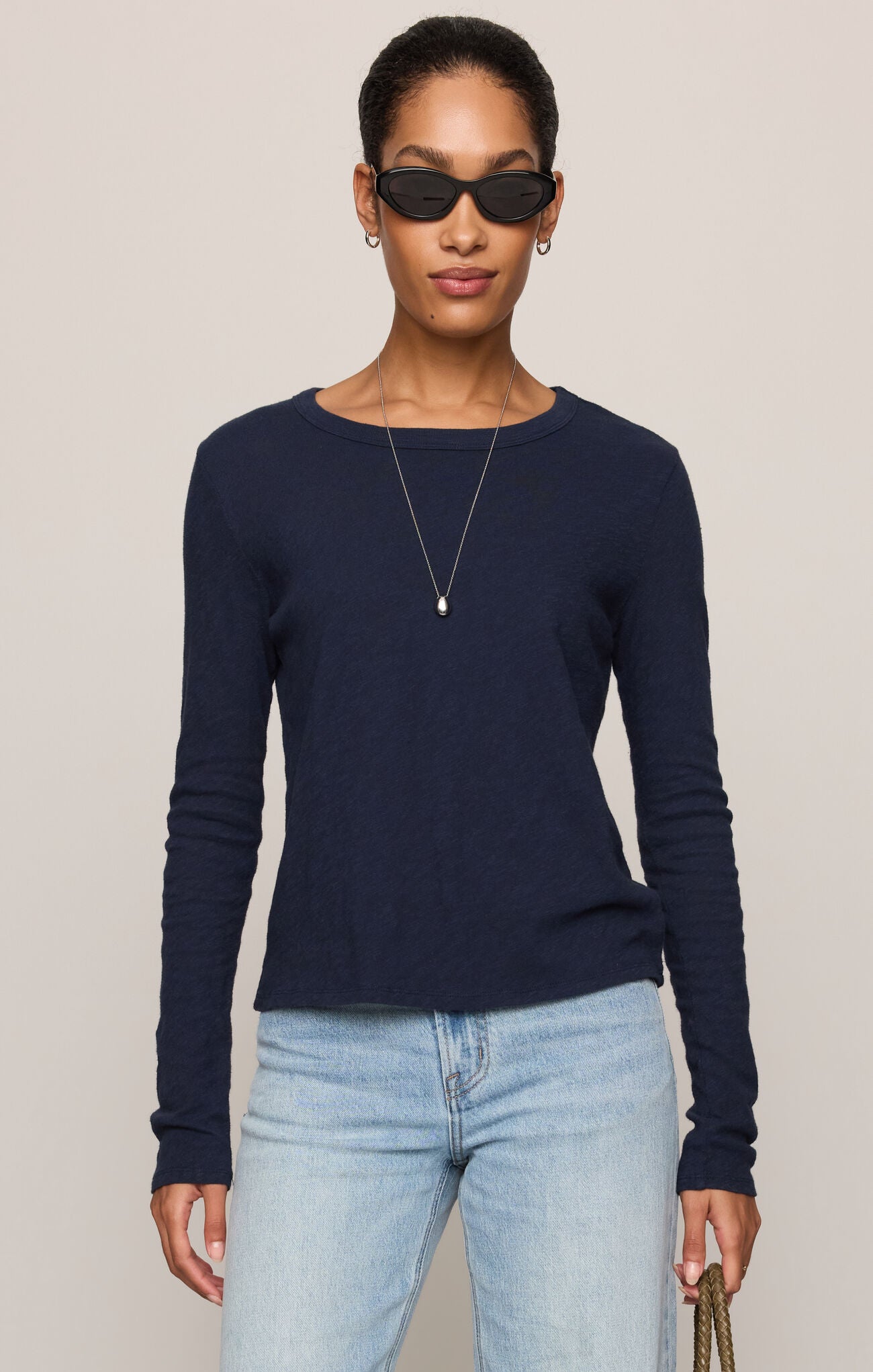 A woman modeling a navy blue long-sleeve knit top with a boat neckline, paired with light blue jeans, against a solid light gray background.